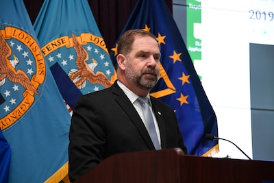 Mike Cannon behind podium with flags in background