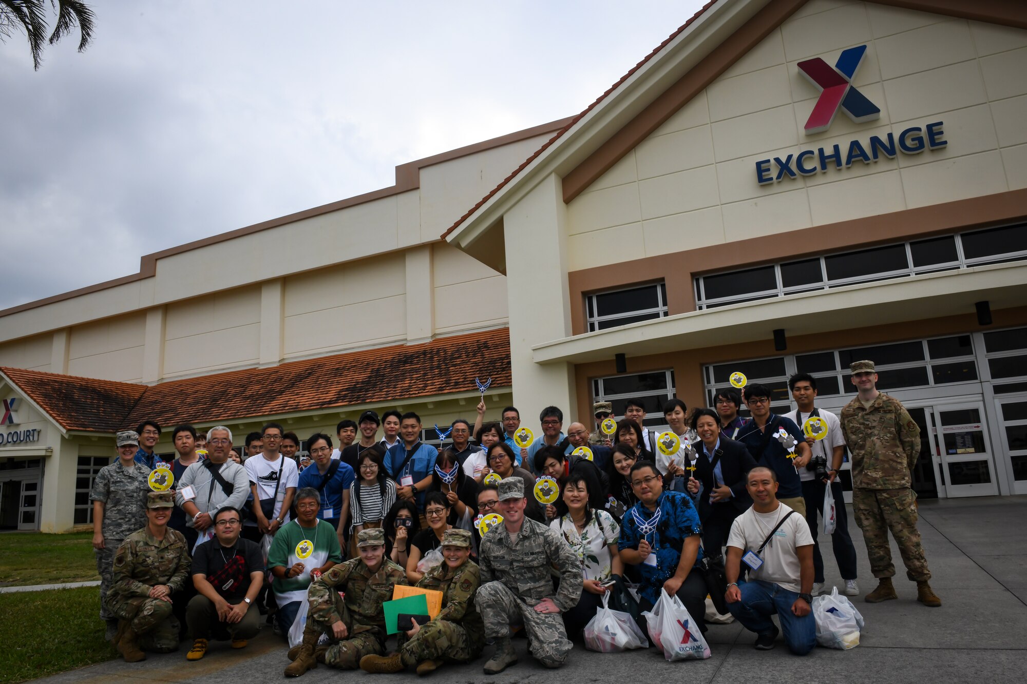 Members from 18th Wing Public Affairs and Twitter Tour visitors pose for a photo in front of the Exchange on Kadena Air Base, Japan, Nov. 4, 2019. During the tour, visitors learned about the 18th Wing misison, security forces partnerships with the Okinawa Prefectural Police, how the base maintains good stewardship of the environment, and Kadena-based aircraft. (U.S. Air Force photo by Staff Sgt. Benjamin Raughton)