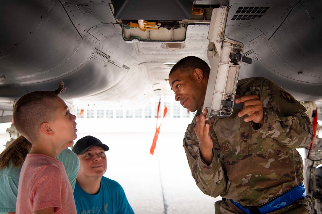 Children look at an airman who is opening a latch underneath an aircraft.