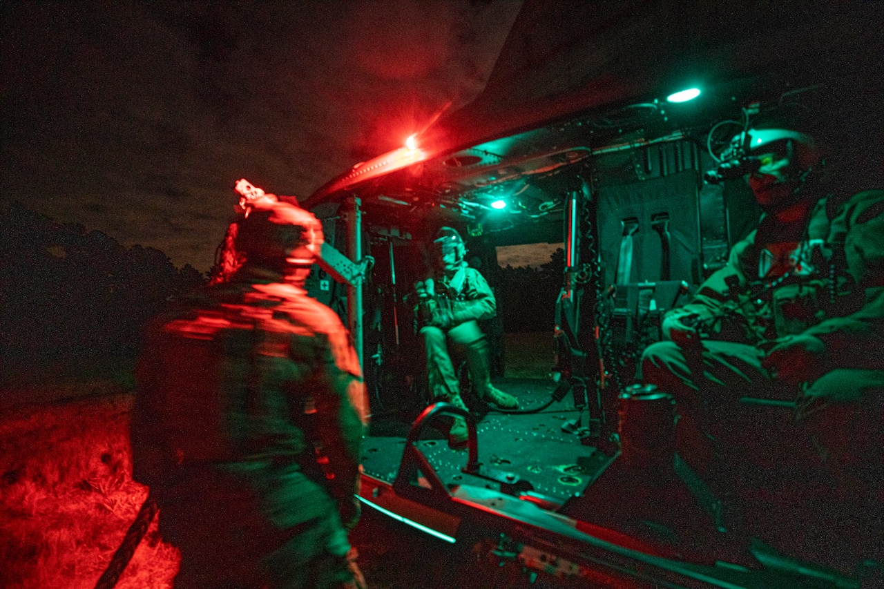 Airmen board a Marine Corps helicopter at night.