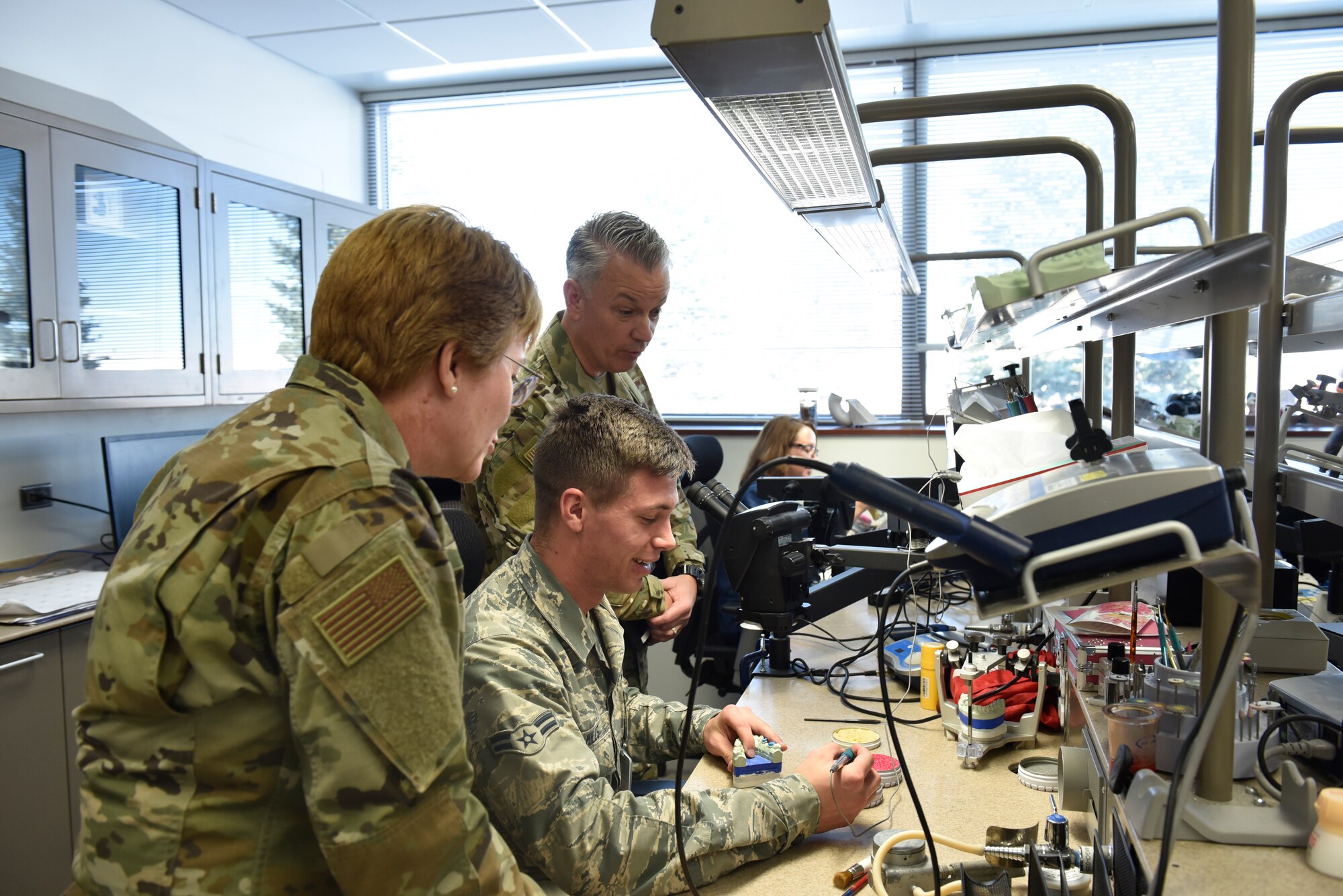 Lt. Gen. Dorothy Hogg, U.S. Air Force Surgeon General, and Chief Master Sgt. Steve Cum, Medical Enlisted Force and Enlisted Corps chief, watch as an Airman works through a dental project at the Area Dental Laboratory on Peterson Air Force Base, Colorado, Nov. 1, 2019. While visiting the Peterson Dental Lab, Hogg and Cum had the chance to see how different molds, implants, and dental pieces are made on a daily basis. (U.S. Air Force photo by Airman Alexis Christian)