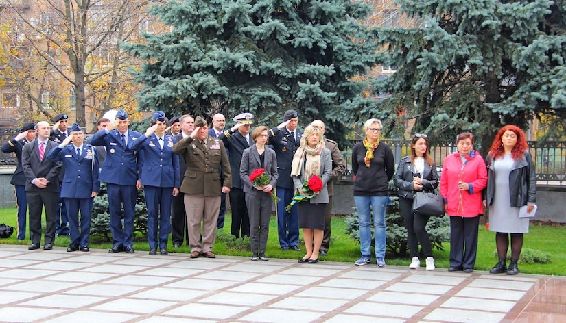 eople in business suits and military uniforms stand in a row facing the camera.