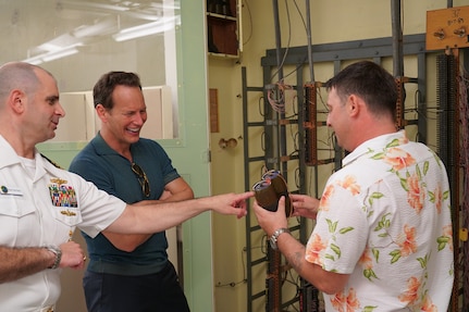 PHNSY&IMF Engineering Technician Noah Green and U.S. PACFLT Director of Intelligence and Information Operations Capt. Tony Butera show actor Patrick Wilson the original 1.2-volt battery used to light up the fiddle board that once intercepted encrypted Japanese intelligence at Station Hypo.