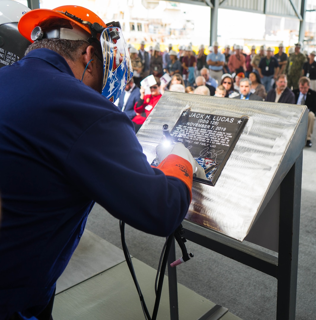 Ingalls Shipbuilding welder James Ellis welds Ship Sponsors Ruby Lucas and Catherine B. Reynolds’ initials into a steel plate during a keel authentication ceremony for the future USS Jack H. Lucas (DDG 125) at Huntington Ingalls Industries Pascagoula shipyard Nov. 7, 2019.