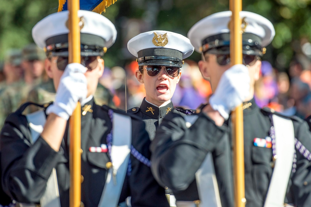 An Army ROTC cadet calls out as two cadets march in front of her.