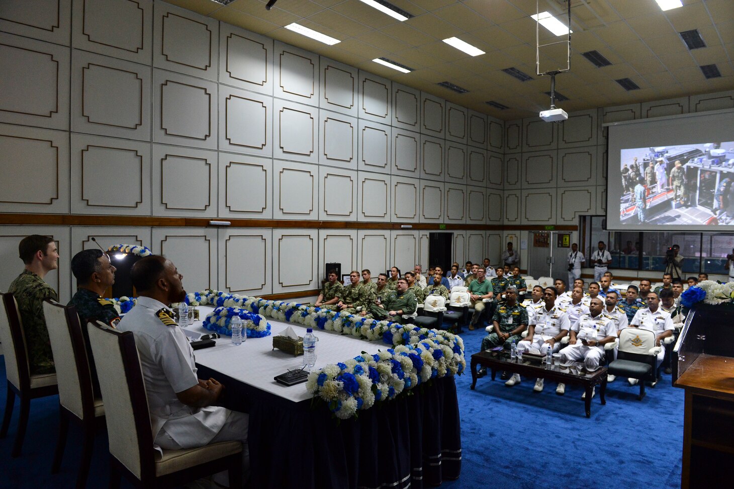 Chattogram, Bangladesh (Nov. 7, 2019) U.S. and Bangladesh Navy Sailors watch a slide show of Cooperation Afloat Readiness and Training (CARAT) Bangladesh 2019 during the closing ceremony for CARAT Bangladesh 2019. This year marks the 25th iteration of CARAT, a multinational exercise designed to enhance U.S. and partner navies' abilities to operate together in response to traditional and non-traditional maritime security challenges in the Indo-Pacific region.