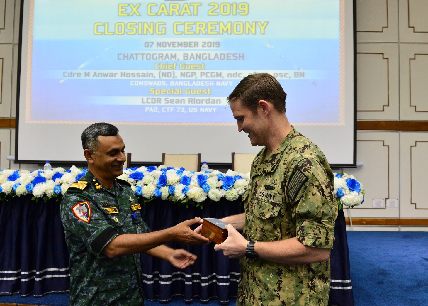 Chattogram, Bangladesh (Nov. 7, 2019) U.S. Navy Lt. Cmdr. Sean Riordan, a representative from Commander, Logistics Group Western Pacific, and Bangladesh Navy Commodore M. Anwar Hossain, exchange gifts during the closing ceremony for Cooperation Afloat Readiness and Training (CARAT) Bangladesh 2019. This year marks the 25th iteration of CARAT, a multinational exercise designed to enhance U.S. and partner navies' abilities to operate together in response to traditional and non-traditional maritime security challenges in the Indo-Pacific region.