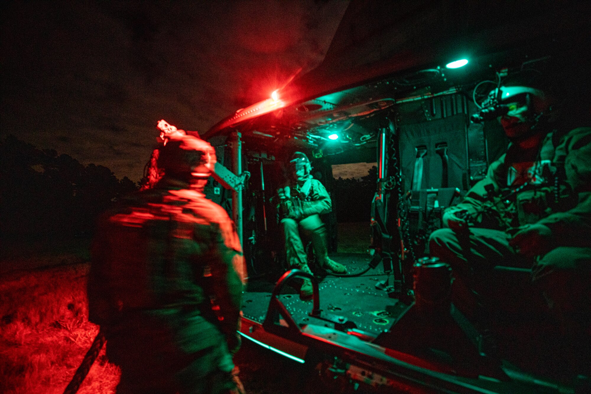 Airmen board a Marine Corps helicopter at night.