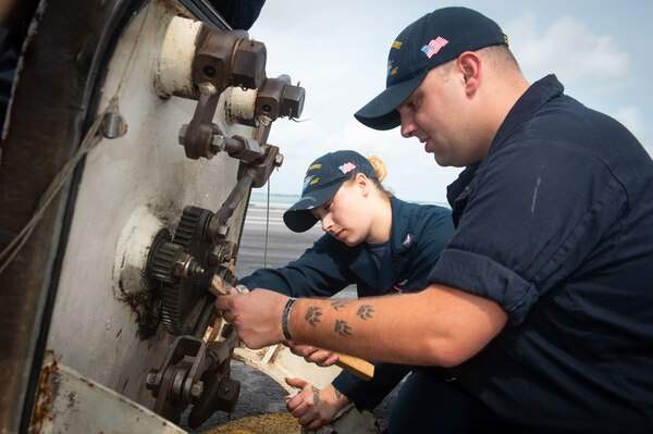 Two sailors work on equipment.