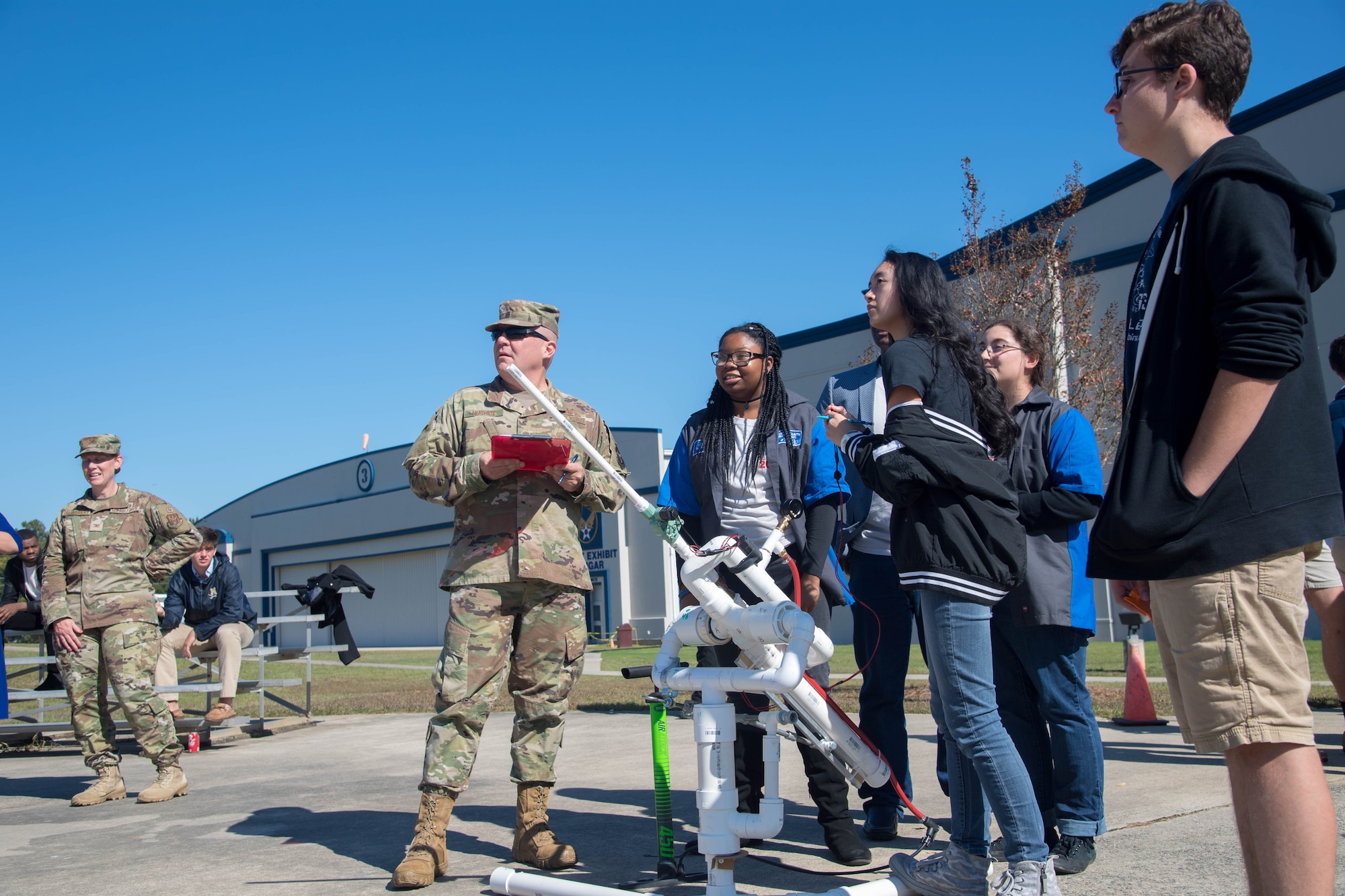 Senior Master Sgt. David Hughes, an inspector general manager at Air Force Reserve Command, grades a team of local high school students on the construction and flight of their model rocket ship made out of paper and other office supplies during a science, technology, engineering, art and science event hosted by AFRC and the Society of American Military Engineers at the Museum of Aviation at Robins Air Force Base, Georgia, Nov. 8, 2019. Students were asked to create a model rocket that could launch to a designated area using air pressure while holding pennies to represent crew and cargo.