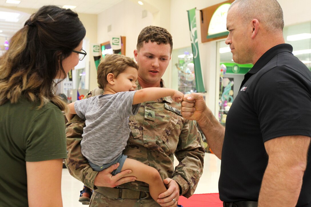 A veteran fist-bumps a young child being held by a service member.