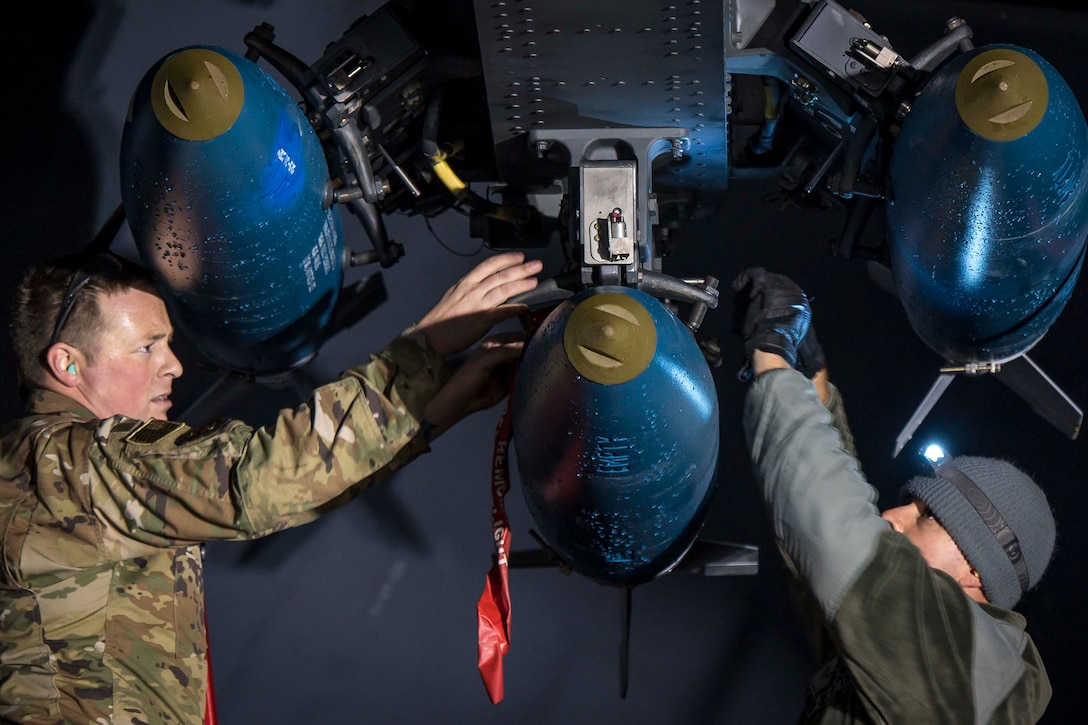 Two airmen attach bombs to an aircraft.