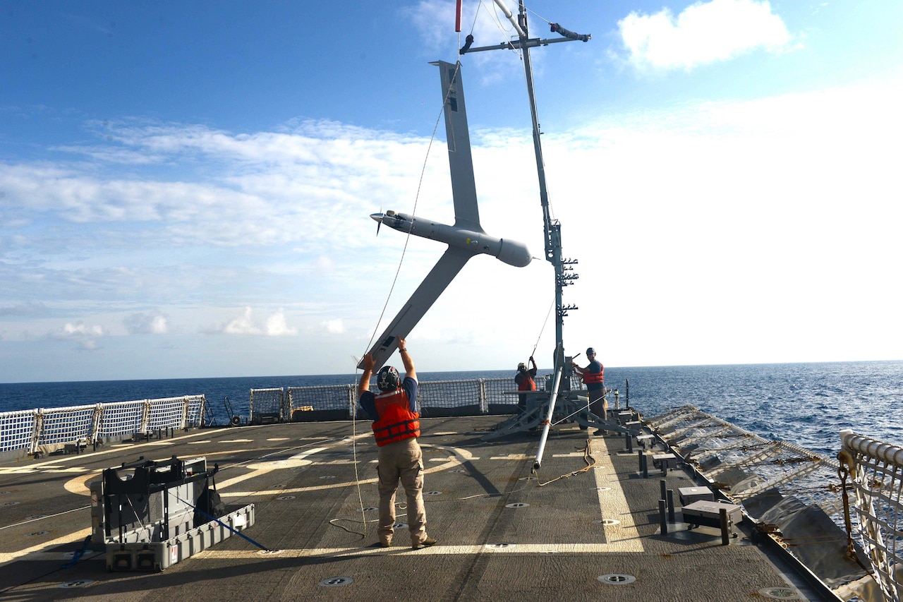 Man holds small airplane on ship at sea.