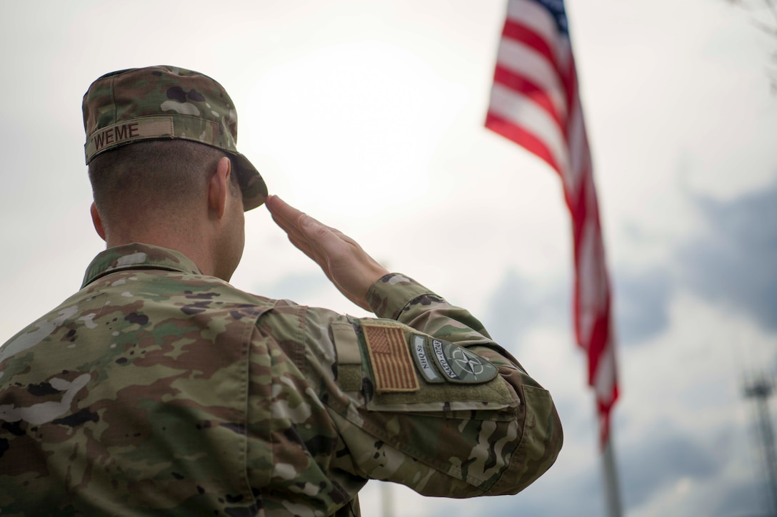 An airman salutes an American flag.