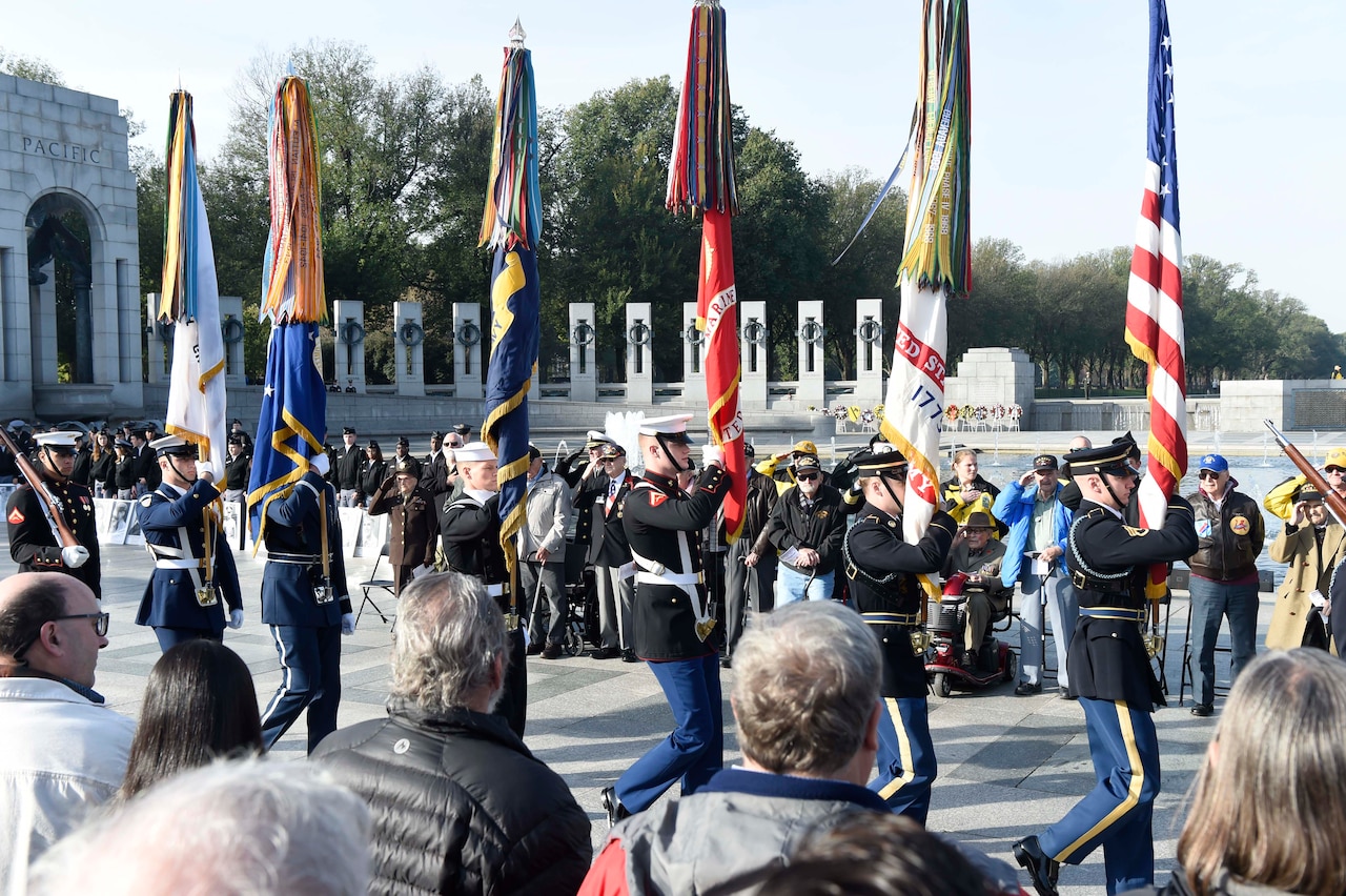 Color guard marches in formation as people salute