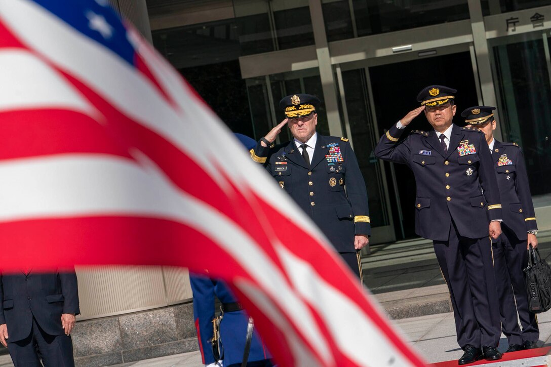 American and Japanese officers stand in the background saluting an American flag waving in the foreground.