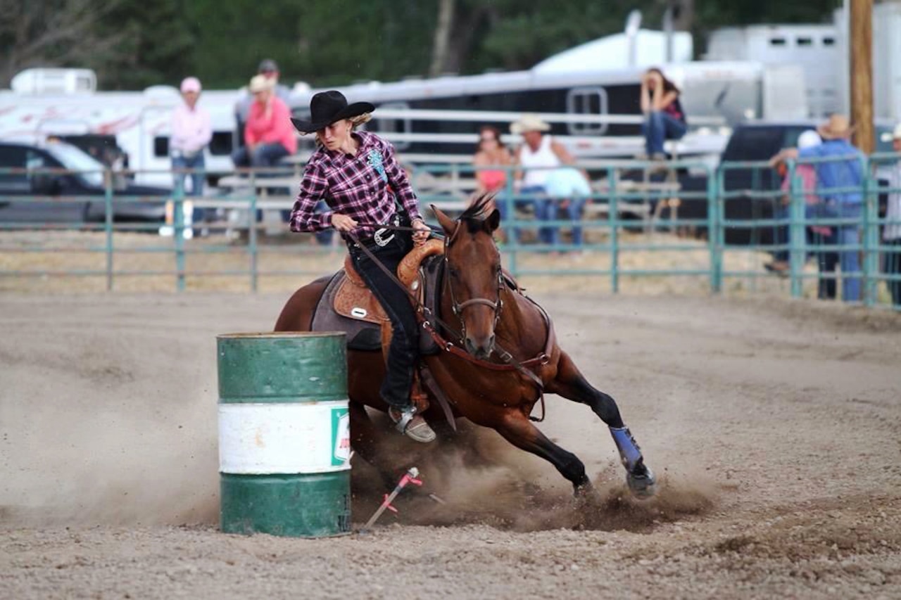 A rider steers a brown horse around a barrel during a rodeo.