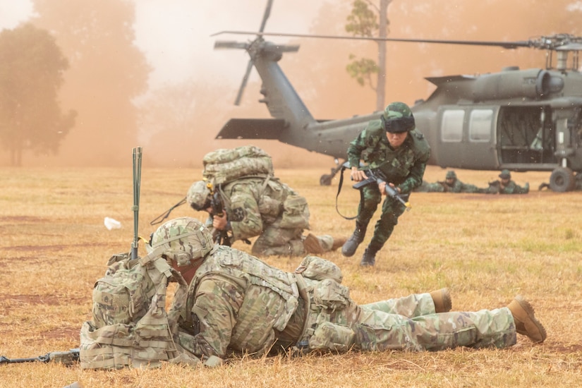 Thai soldier runs from a helicopter to join crouching U.S. soldiers during an air assault training mission.