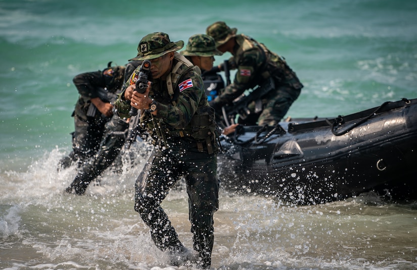 Thai Marines wade ashore from a rubber landing craft. The lead Marine aims a rifle.