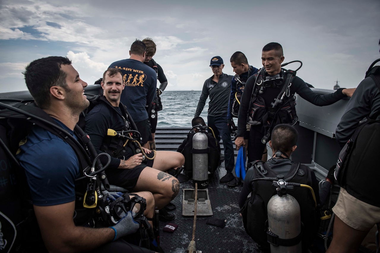 Sailors wearing diving gear talk on the deck of a boat.