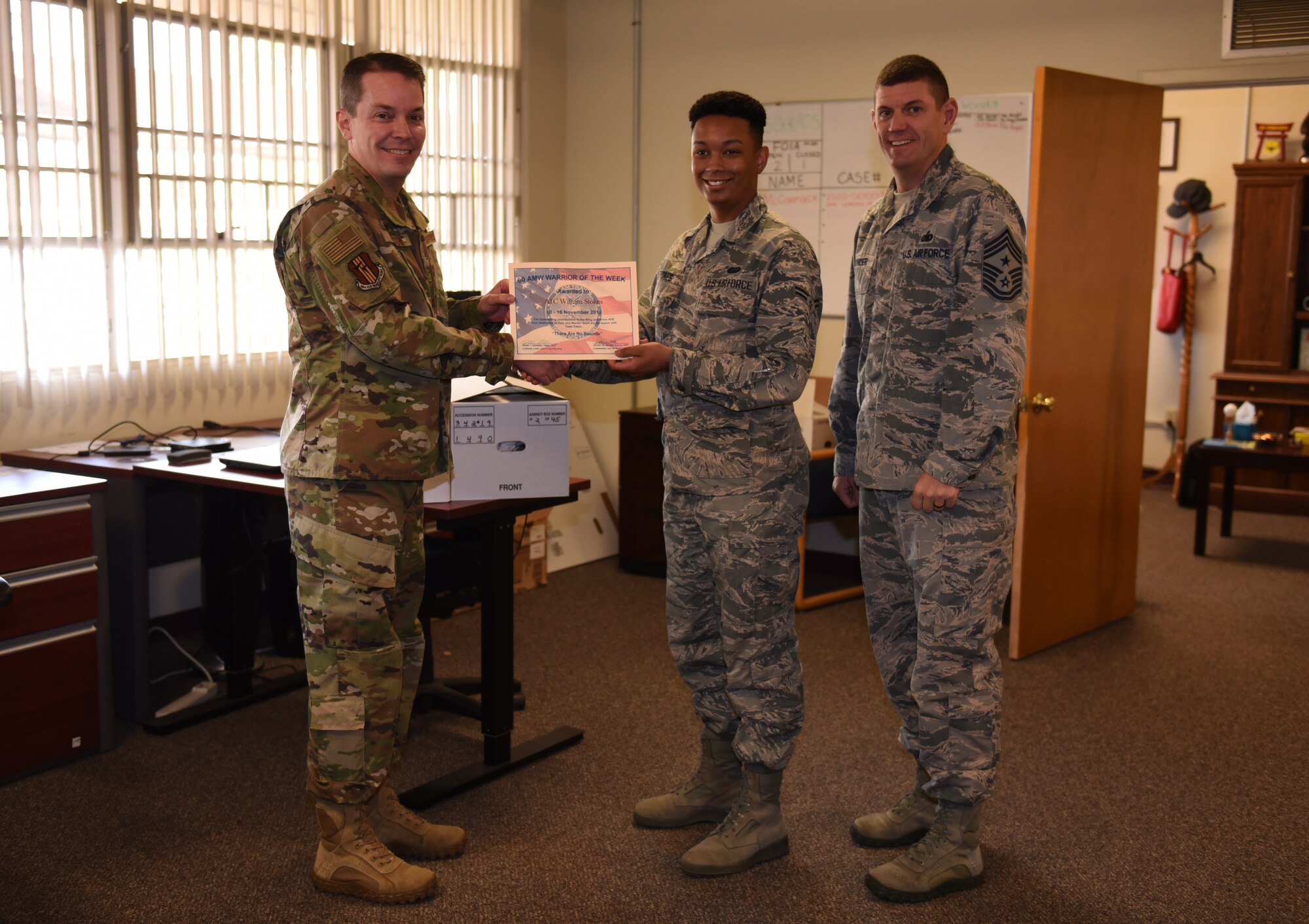 U.S. Air Force Airman 1st Class William Stokes, center, 60th Communications Squadron knowledge management technician, is recognized by Col. Jeffrey Nelson, left, 60th Air Mobility Wing commander, and Chief Master Sgt. Derek Crowder, right, 60th AMW command chief, as Warrior of the Week Nov. 12, 2019, at Travis Air Force Base, California. Stokes was recognized as the WoW for Nov. 10-16. The program highlights a Travis Airman for his or her outstanding performance. (U.S. Air Force photo by Airman 1st Class Cameron Otte)