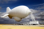 White blimp is filled with helium against a blue sky and clouds