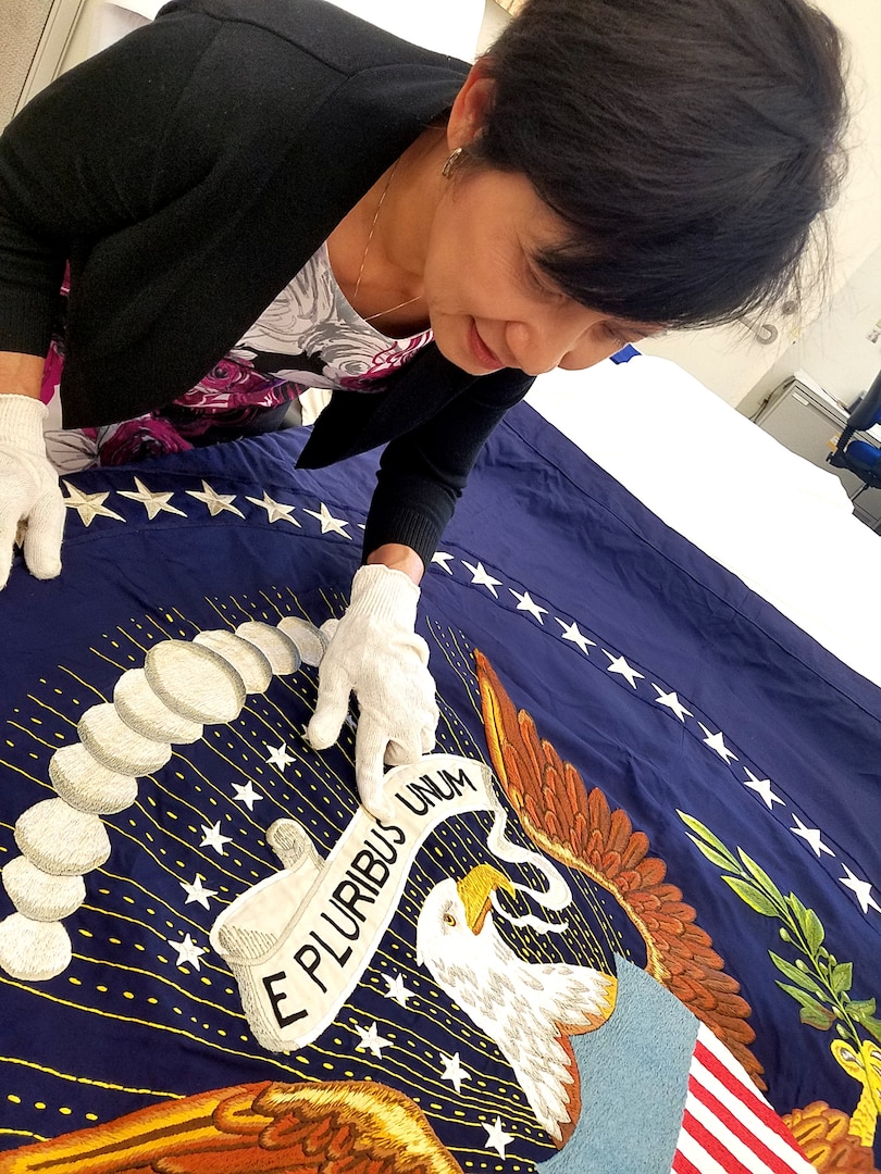 Woman wearing white gloves inspects a U.S. presidential flag.