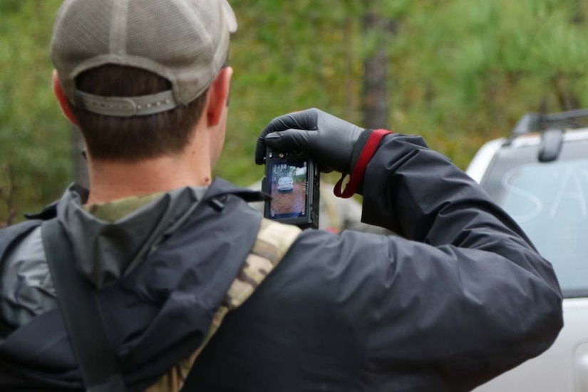 Photo of a man from the back; he is holding a device with a small screen in one hand.