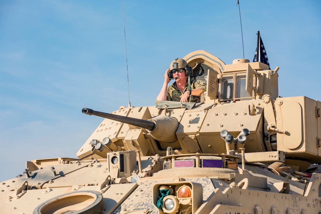 A soldier looks out from the top of a Bradley Fighting Vehicle.
