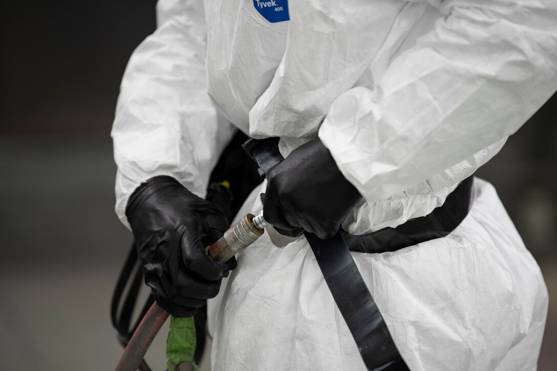 A photo of an Airman connecting an air line to his mask before painting an aircraft part