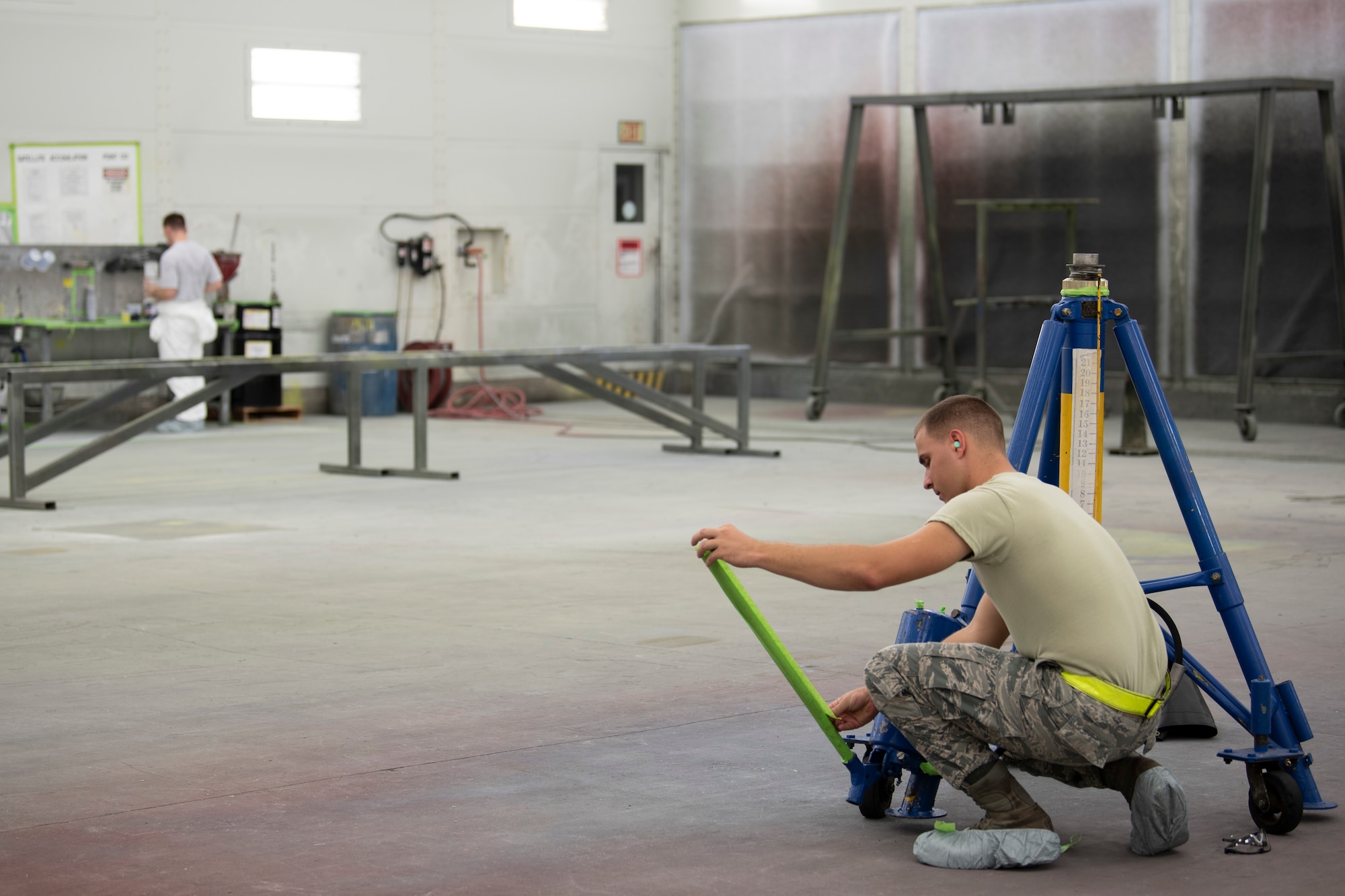 A photo of an Airman masking part of a jack stand before painting