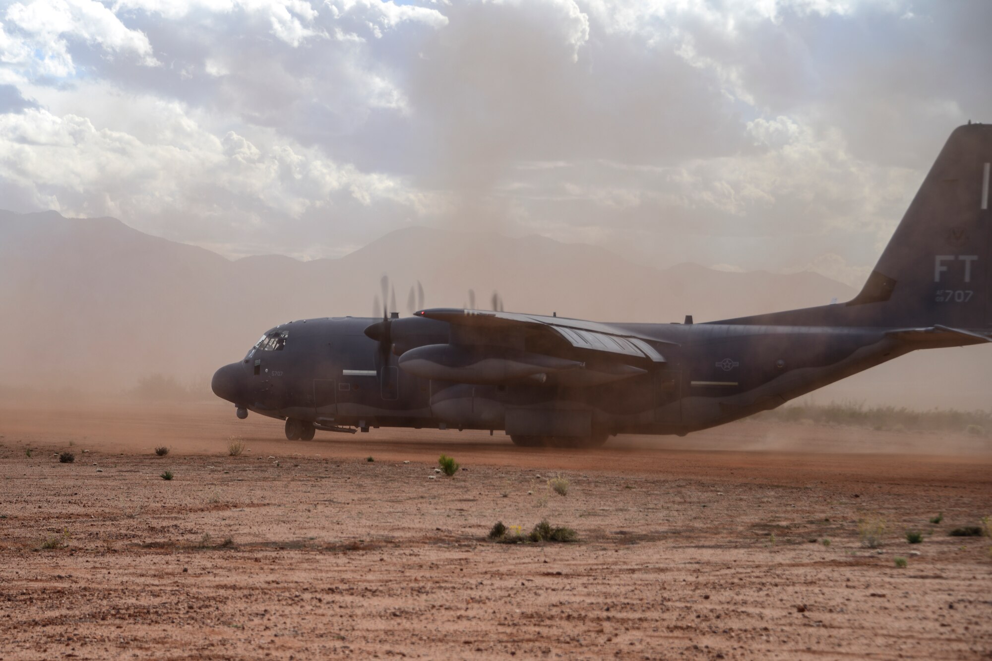 A photo of an HC-130J parked on a dirt runway.
