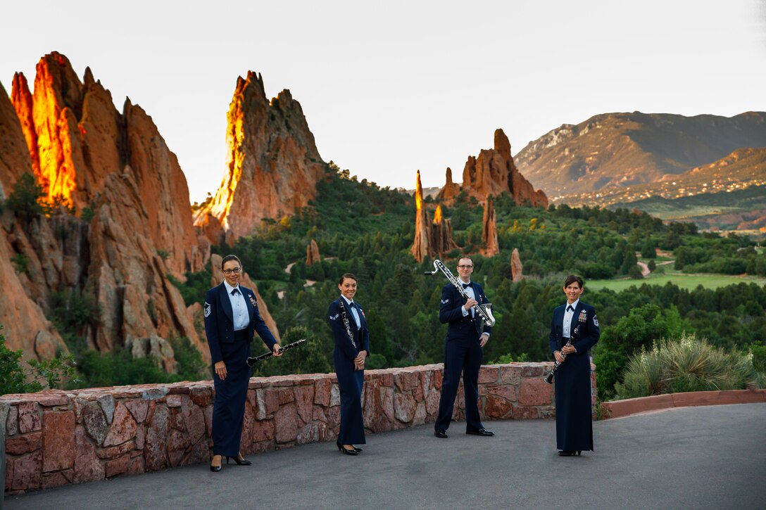 Four clarinetists wearing their dark blue mess dress uniforms stand in front of a vista of rock formations and mountains, holding their instruments as the morning light makes the red rocks glow.