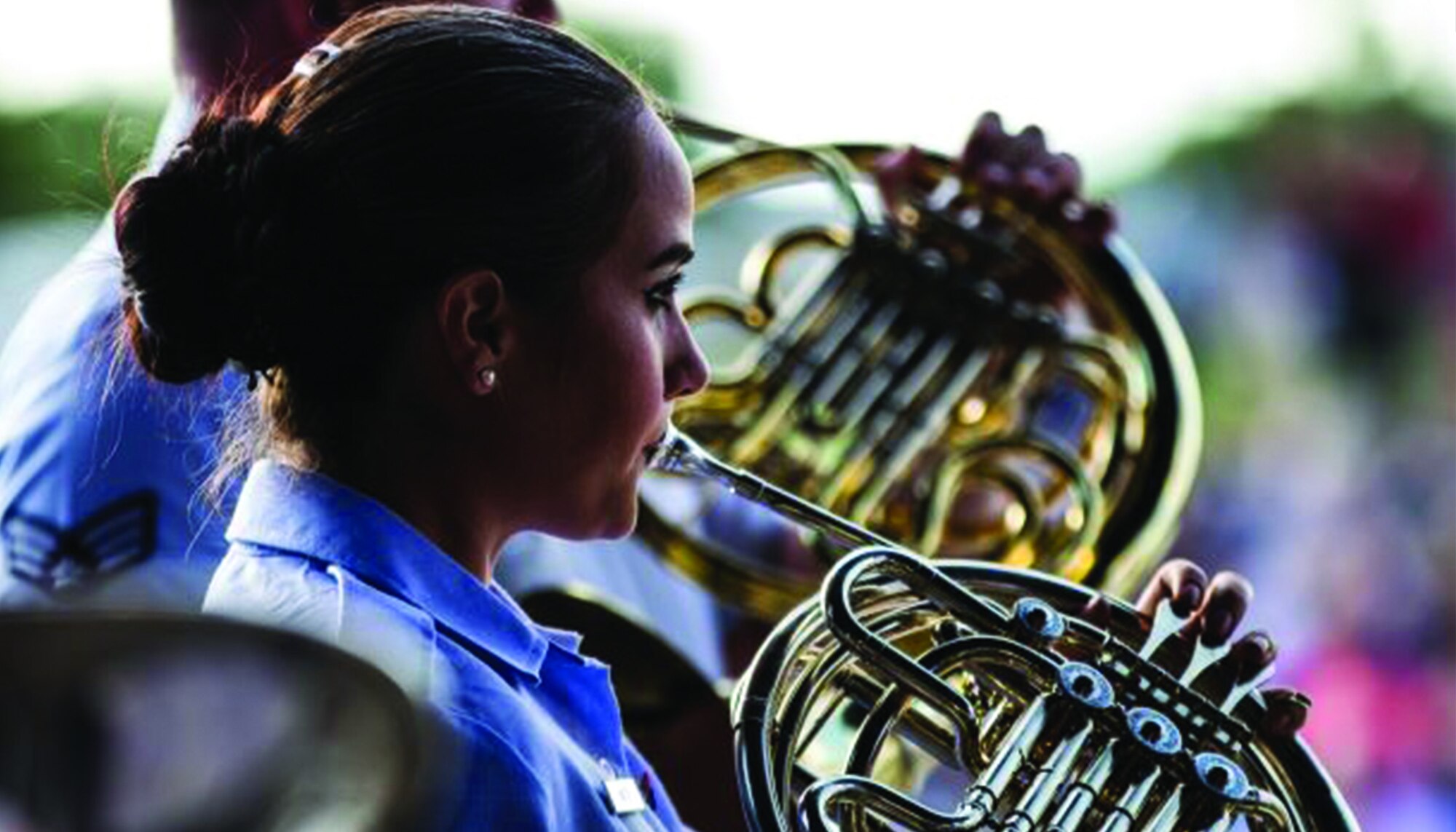 An Academy Band French horn player performs in her blue uniform during a 2019 concert band Independence Day tour.