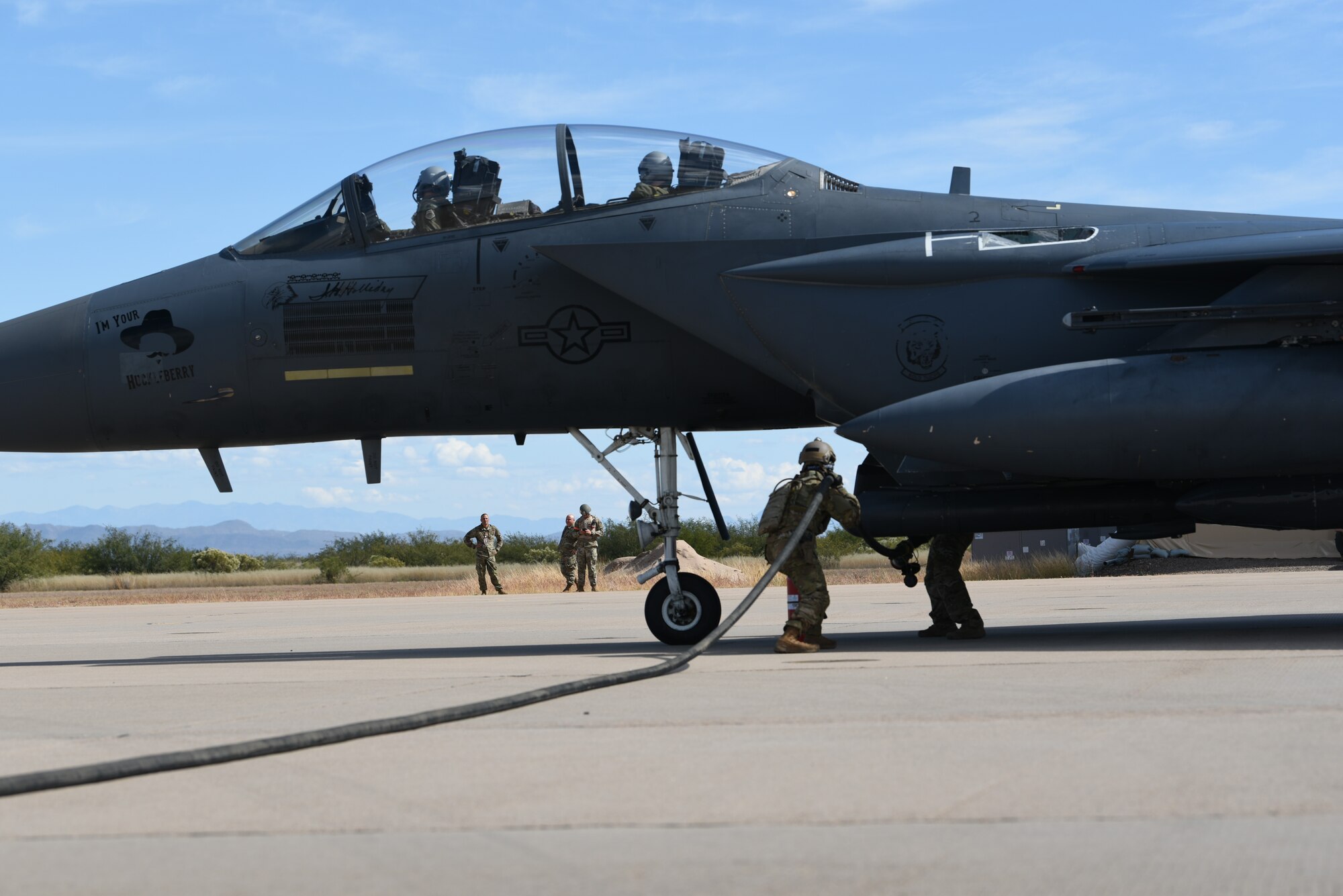 A photo of airmen working on an F-15 parked on a runway.