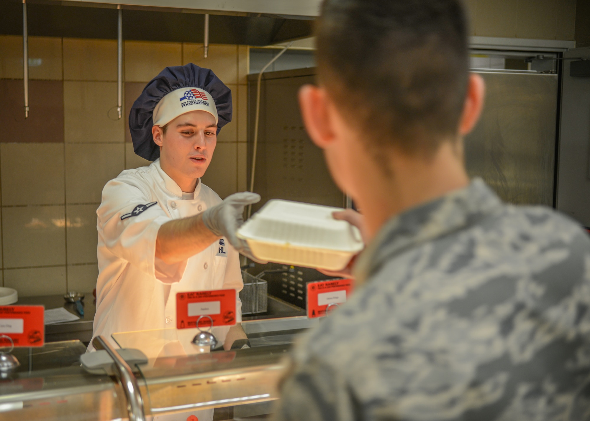 U.S. Airman Kellan S. Hill, 31st Force Support Squadron server, hands an Airman their order at the La Dolce Vita dining facility, Aviano Air Base, Italy, Nov. 7, 2019. La Dolce Vita offers numerous specialty meals to include Airman Appreciation meals, Mongolian, and Pancake Extravaganzas, as well as celebrating all national holidays including Thanksgiving and Christmas. (U.S. Air Force photo by Airman Thomas S. Keisler IV)