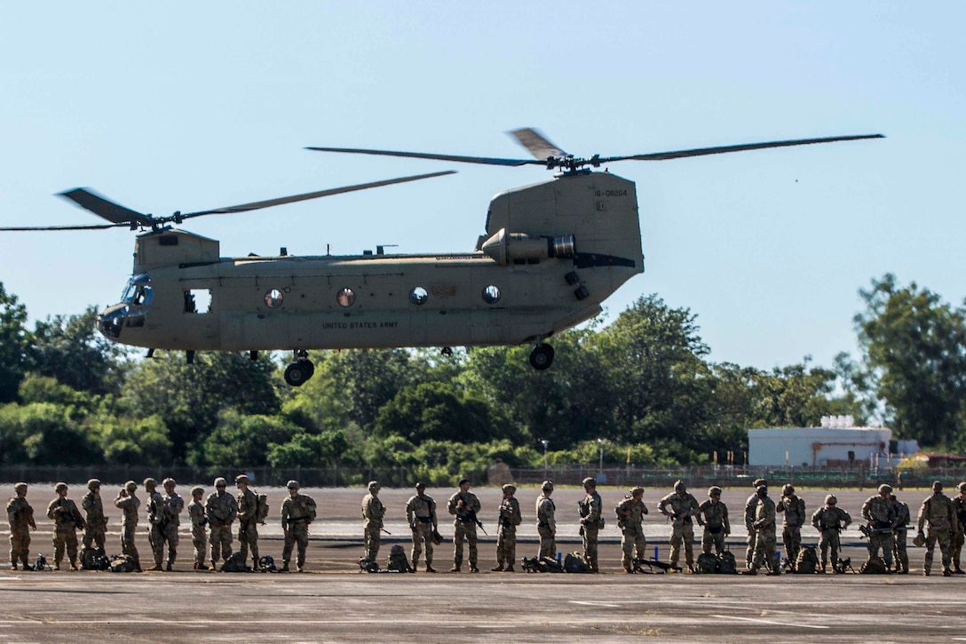 A group of soldiers stand underneath a helicopter.