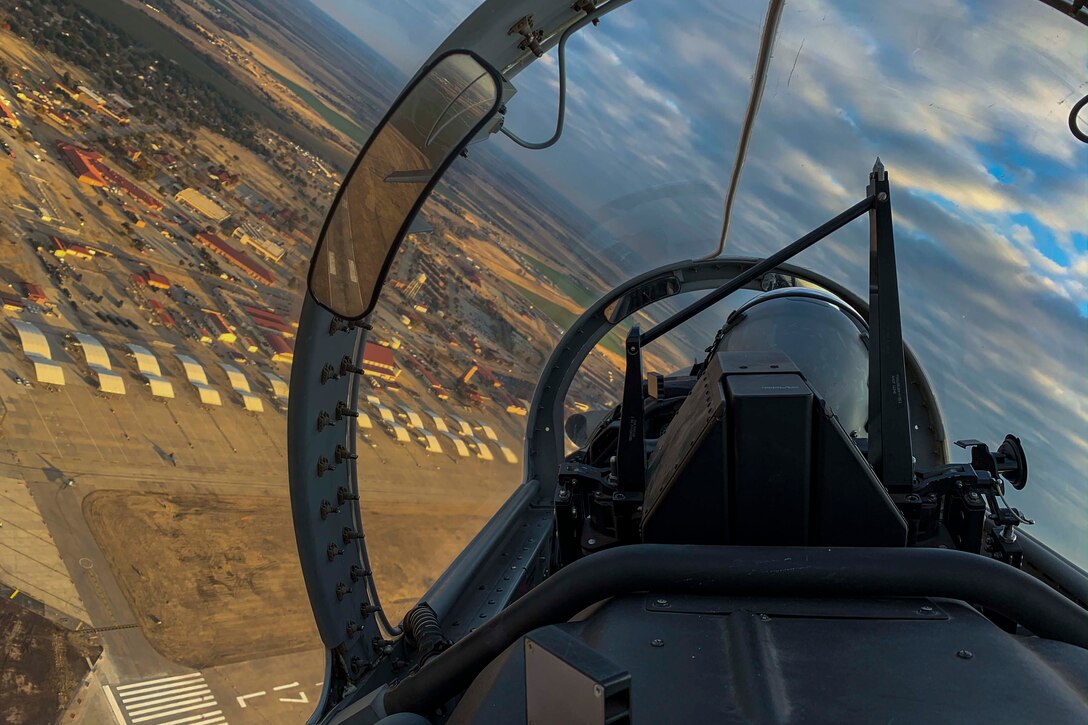 An airman sits in a cockpit while flying over a city.