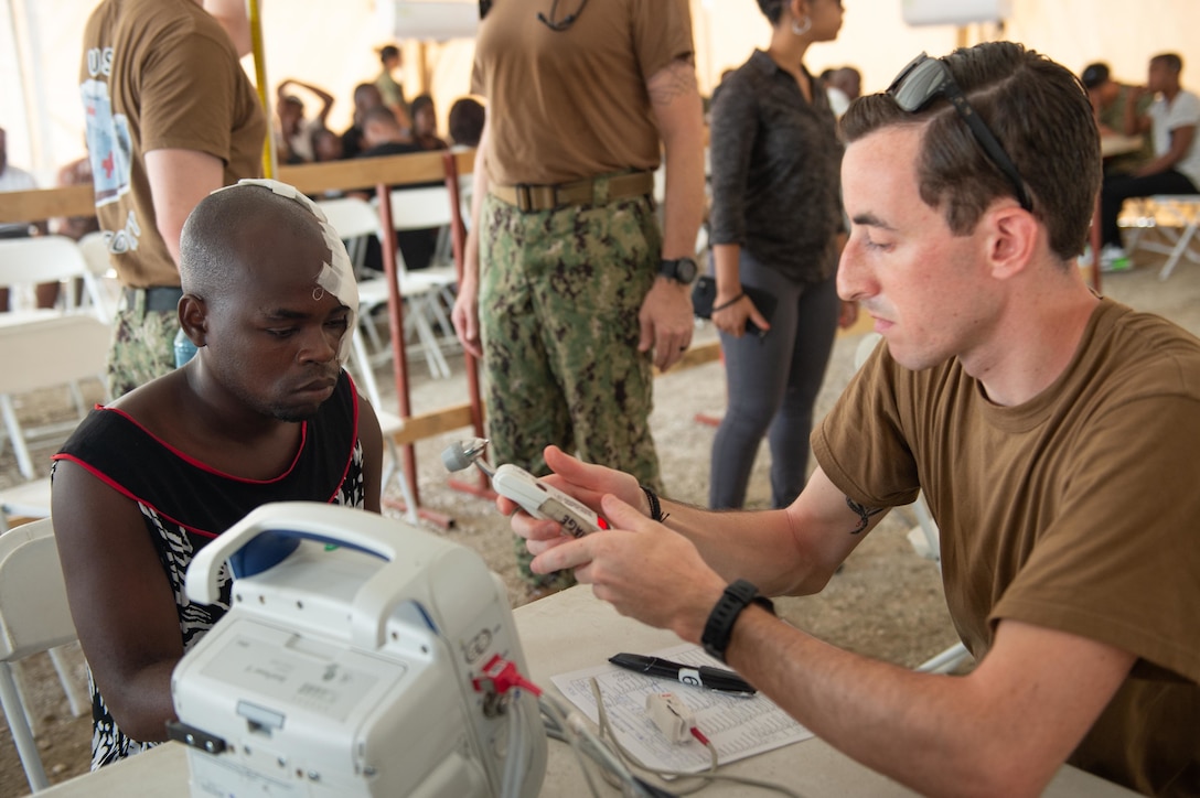 U.S. Navy Hospitalman Adam Lee, assigned to the hospital ship USNS Comfort (T-AH 20), checks the vital signs of a man who has multiple lacerations from a motorcycle accident at a temporary medical treatment site in Port-Au-Prince, Haiti, Nov. 6, 2019.