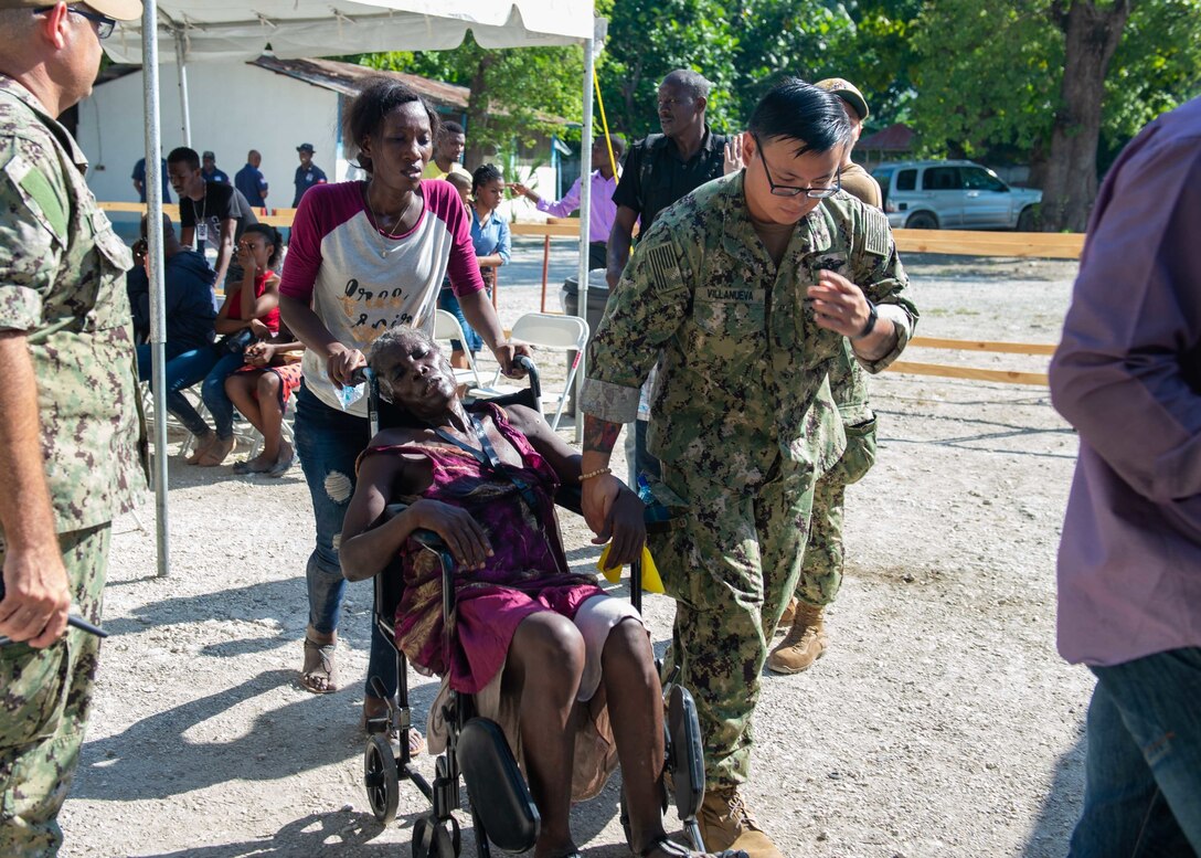 U.S. Navy Hospitalman Jonathan Villanueva, assigned to the hospital ship USNS Comfort (T-AH 20), escorts a woman with abdominal pain to be seen by medical staff at a temporary medical treatment site in Port-Au-Prince, Haiti, Nov. 6, 2019.