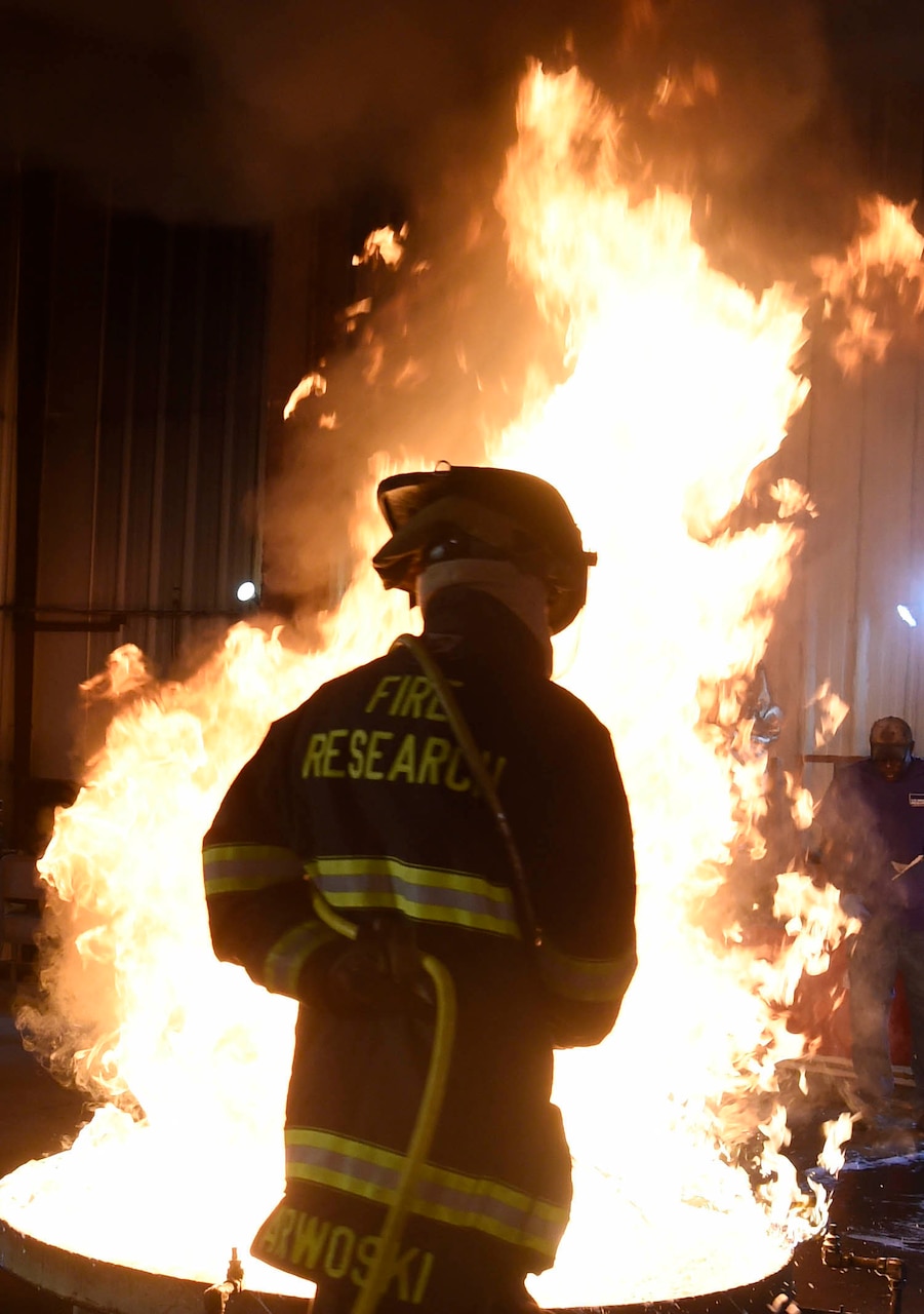 A person wearing fire protection gear sprays foam on a fire in a 28-square-foot container.