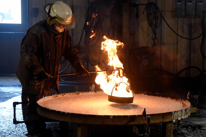 A person wearing fire protection gear sprays foam on a fire in a 28-square-foot container.