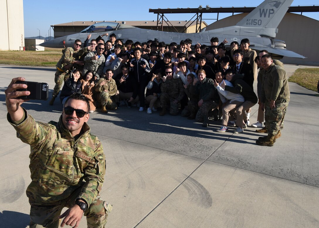 U.S. Air Force Staff Sgt. John Lace, 8th Aircraft Maintenance Squadron dedicated crew chief, takes a selfie with a group of students from Gunsan Dong High School at Kunsan Air Base, Republic of Korea, Nov. 8, 2019. Lace spoke to the students about the capabilities of the F-16 Fighting Falcon including its cost, payload and his role in the repair of the aircraft. (U.S. Air Force photo by Staff Sgt. Anthony Hetlage)