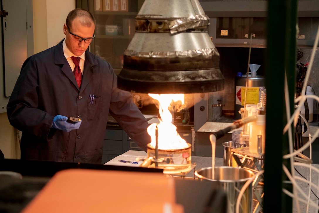 A chemist holds a stopwatch as he times an experiment of a small fire in a lab.