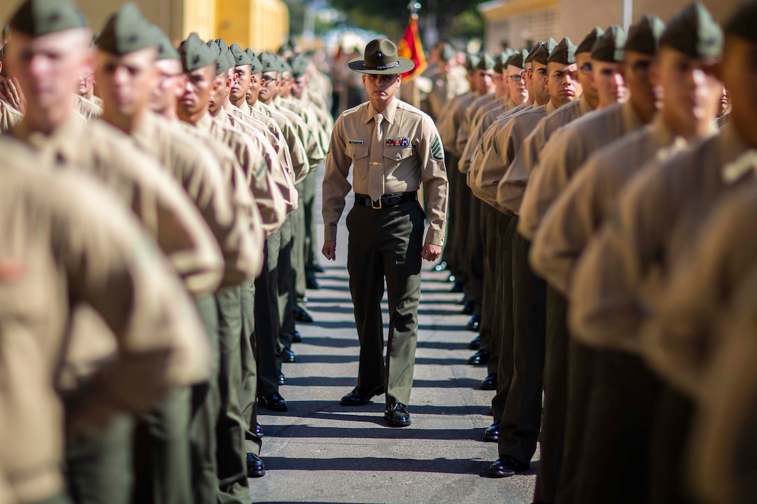 A Marine walks in between a large group of Marines standing in rows.