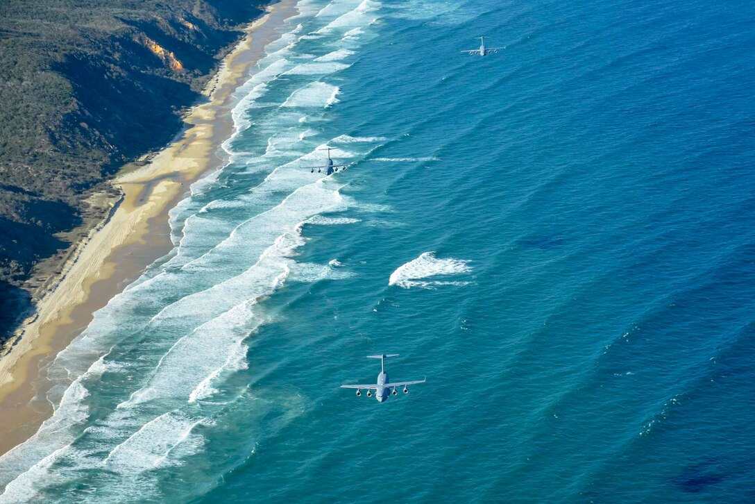 Three planes fly over a beach.