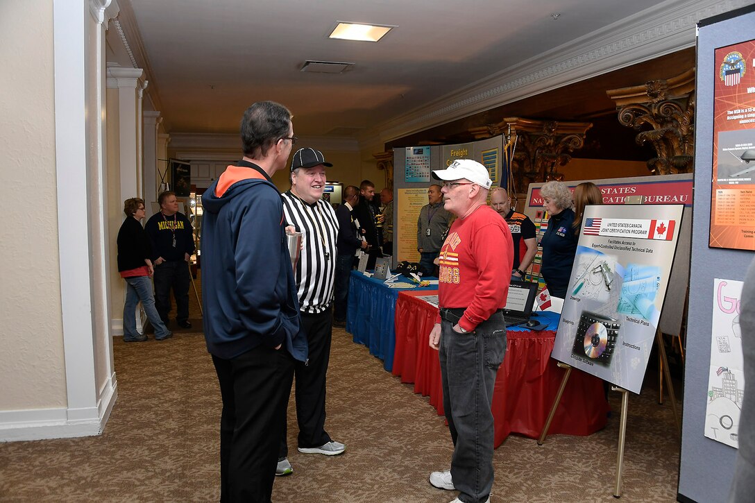 Three men talk in front of a display booth