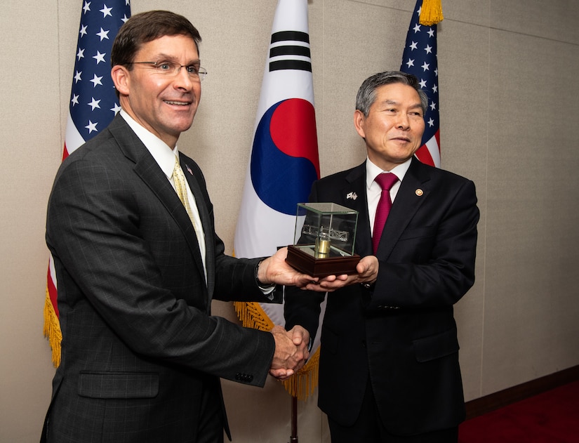 Two men shake hands and hold a glass box.