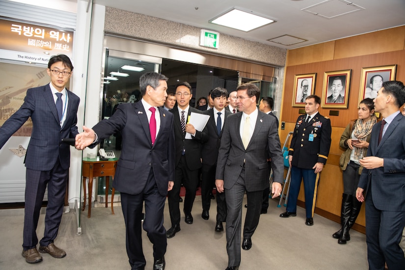 Two men surrounded by a bunch of people walk through a doorway.