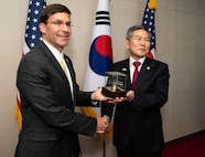 Two men shake hands and hold a glass box.